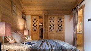 Un dormitorio acogedor con techo de madera, una cama con colcha estampada, una lámpara de noche y un armario con puertas persianas.