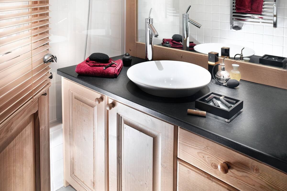 Un baño moderno con tocador de madera, un espejo grande, un lavabo redondo y zona de ducha.