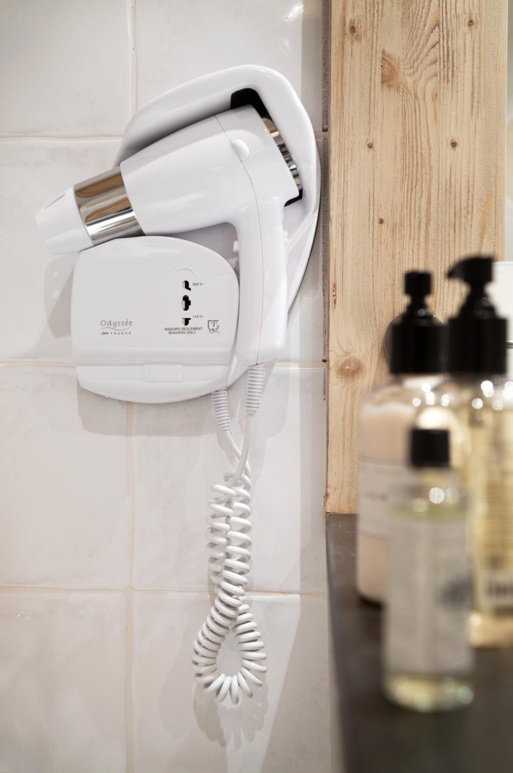 A white hairdryer and phone on a tiled wall, with wooden paneling and bottles of toiletries nearby.