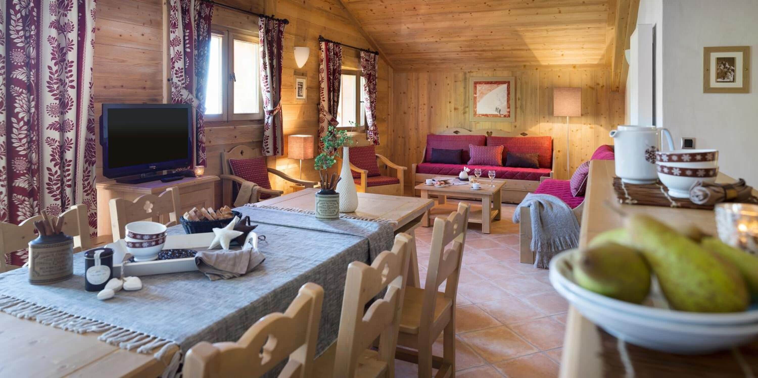 L’intérieur chaleureux d’un chalet avec une table à manger en bois, des chaises, un canapé et un téléviseur.