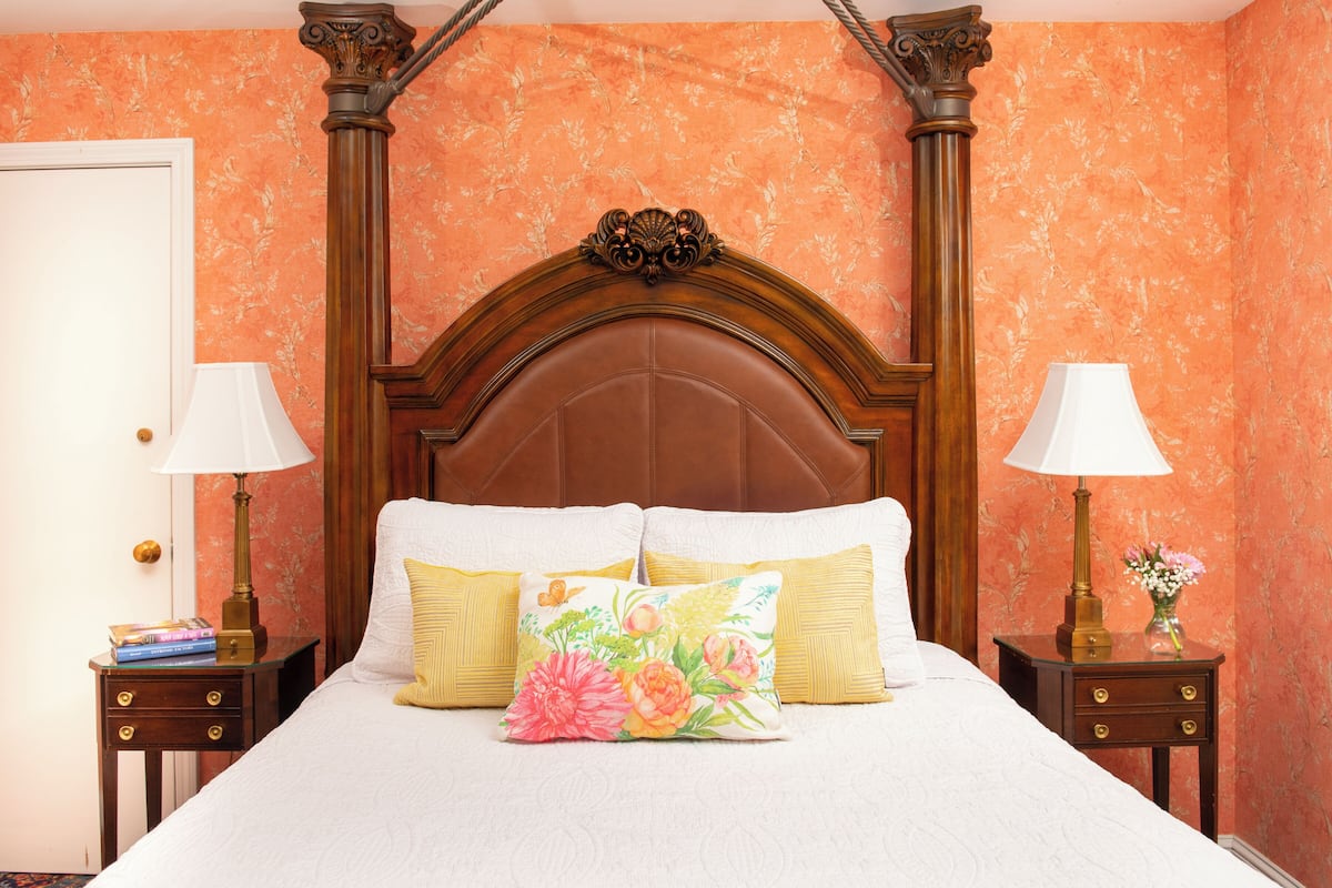 A neatly made bed with floral pillows, a wooden headboard, and two bedside tables with lamps and books.