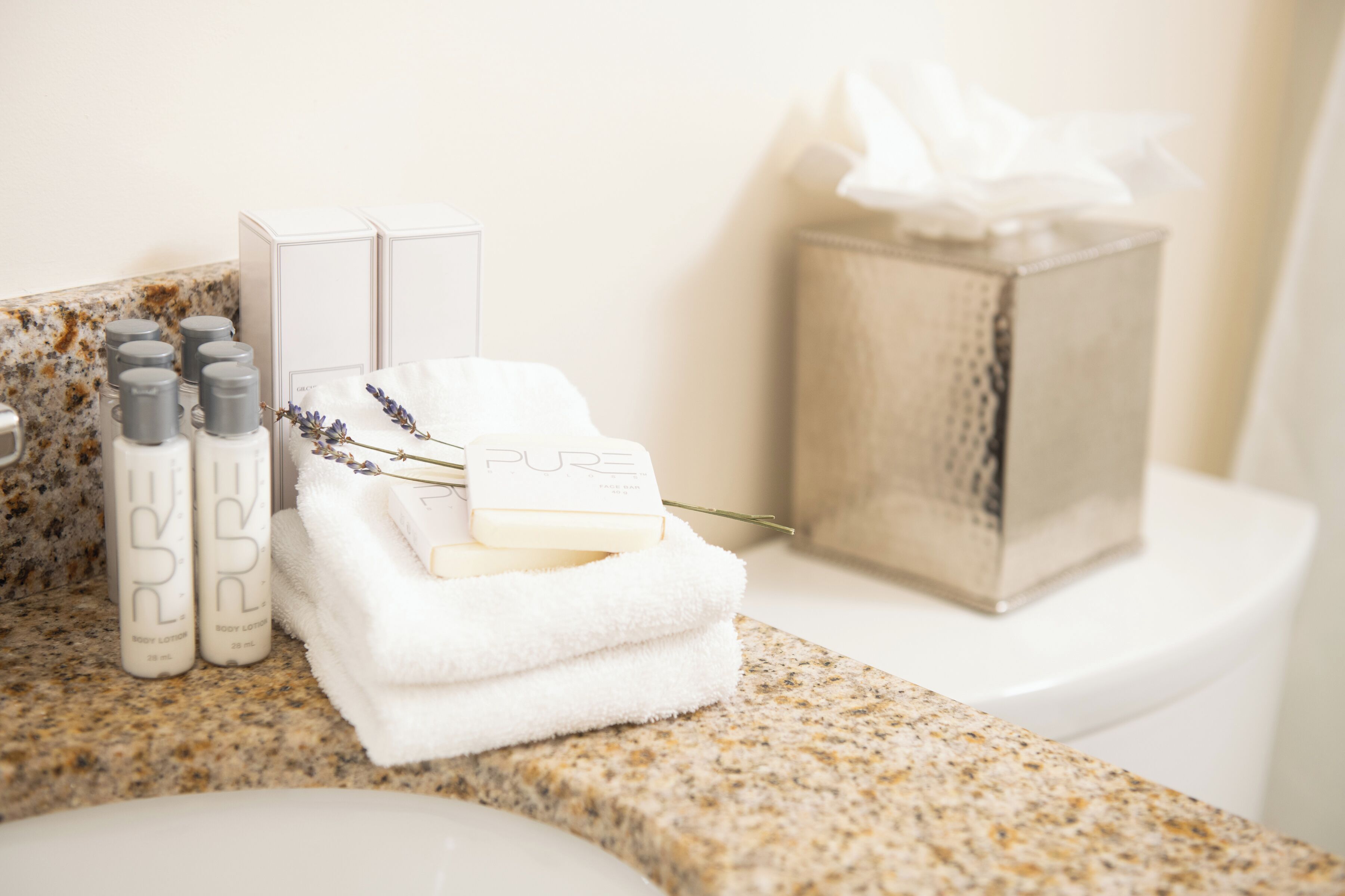 Un tocador de baño con encimera de granito, una toalla blanca y dos botellas de crema corporal con la etiqueta "PURE".