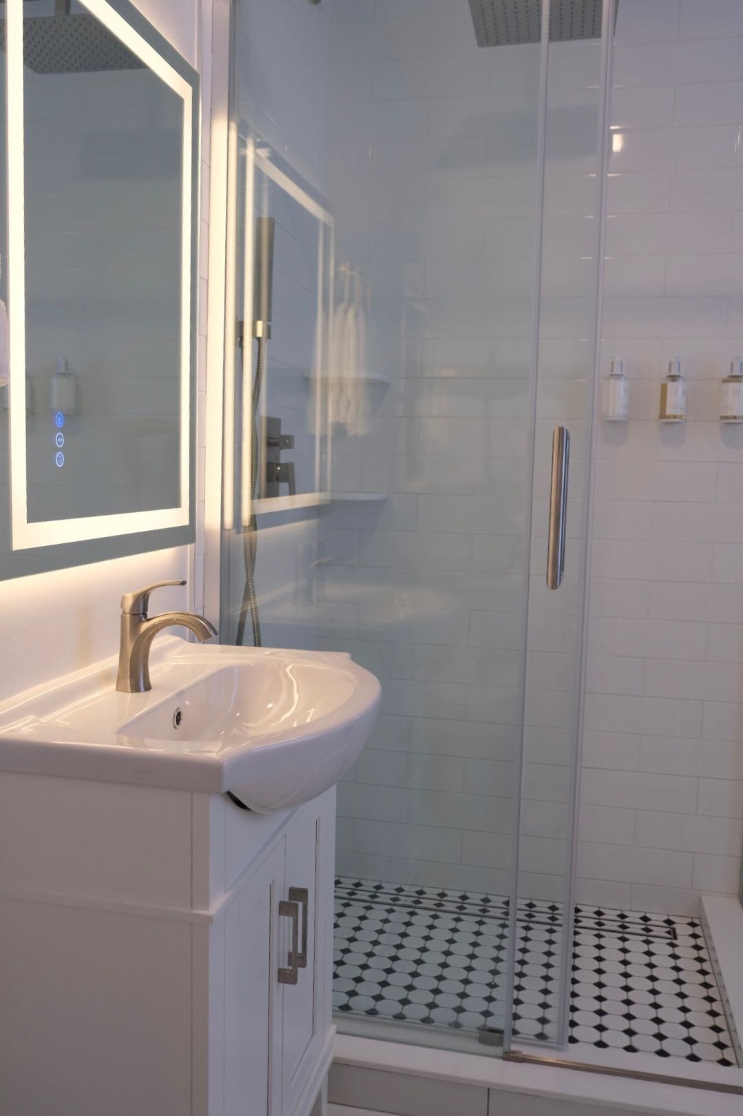 A modern bathroom with a glass-enclosed shower, a white sink with a mirror, and a tiled floor.