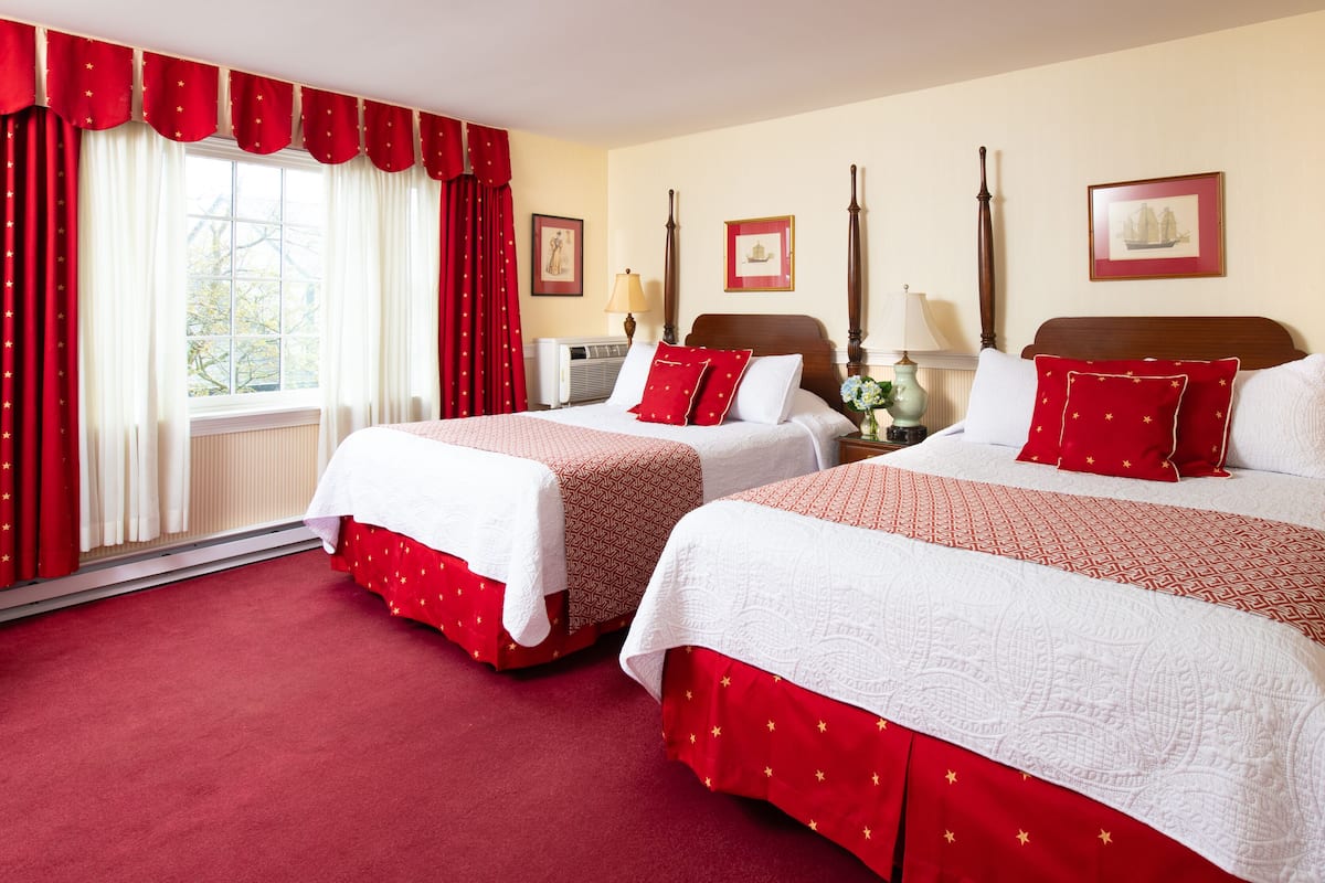 A hotel room with two beds, red curtains with stars, a large window, and framed pictures on the wall.