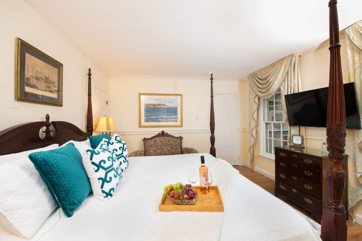 A hotel room with a bed, a wooden dresser, a television, and a window with curtains.