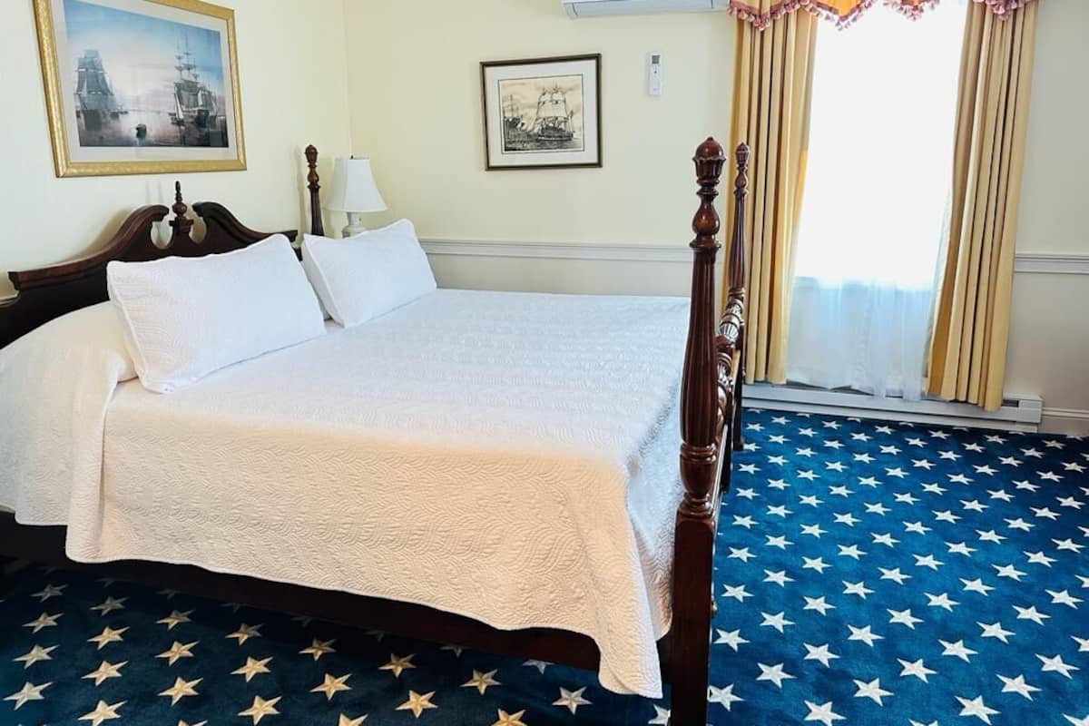 A neatly made bed with white linens, a wooden headboard, and a blue carpet with star patterns.