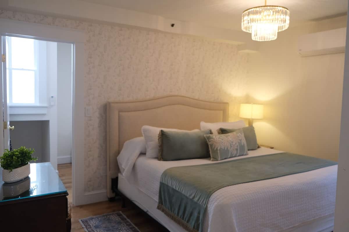 A bedroom with a bed, a nightstand, a lamp, and a chandelier.