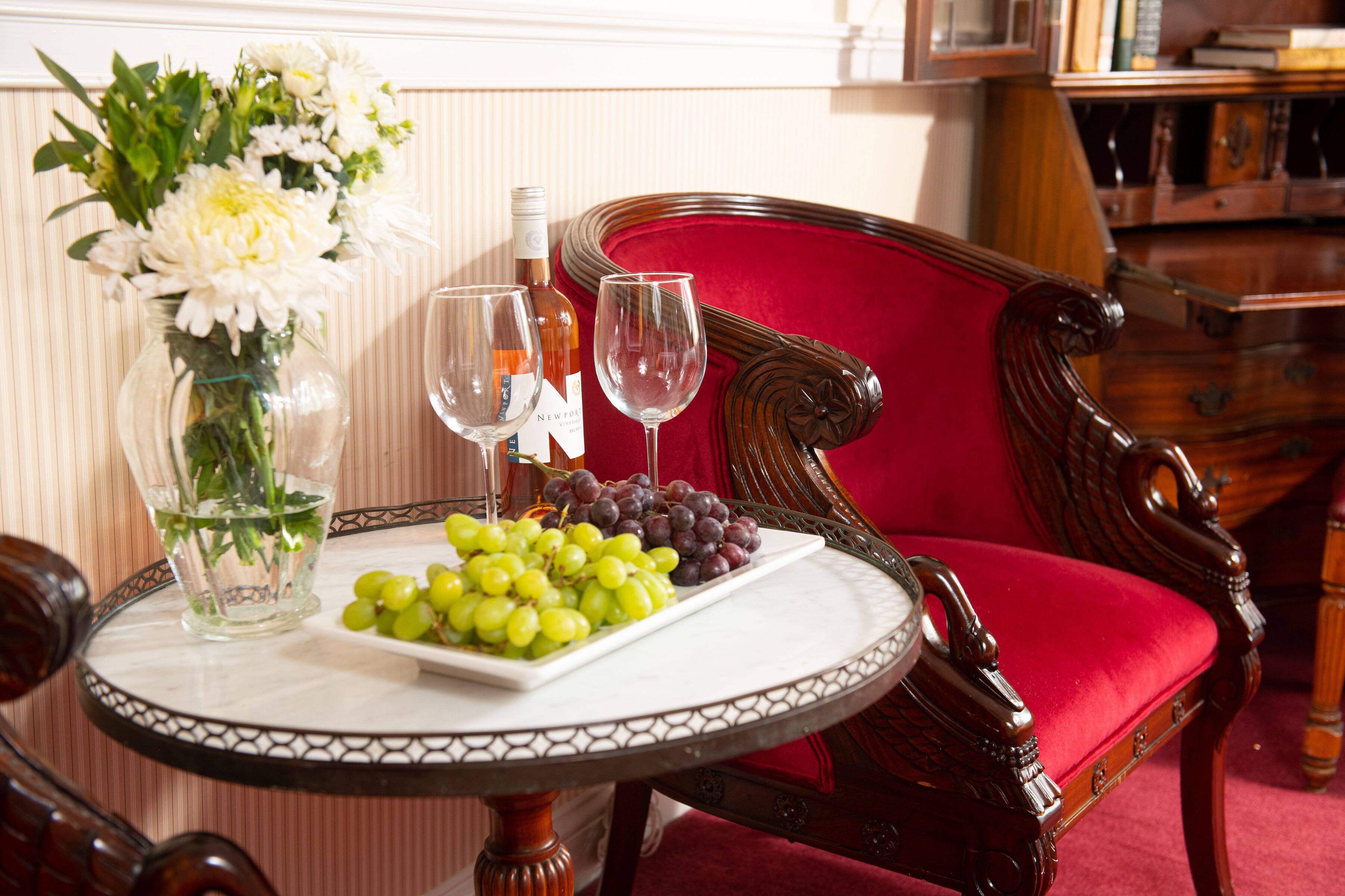 Een eettafel met een zwart-wit geruit tafelkleed, een vaas met witte bloemen, een fles wijn, twee wijnglazen en een schaal druiven.