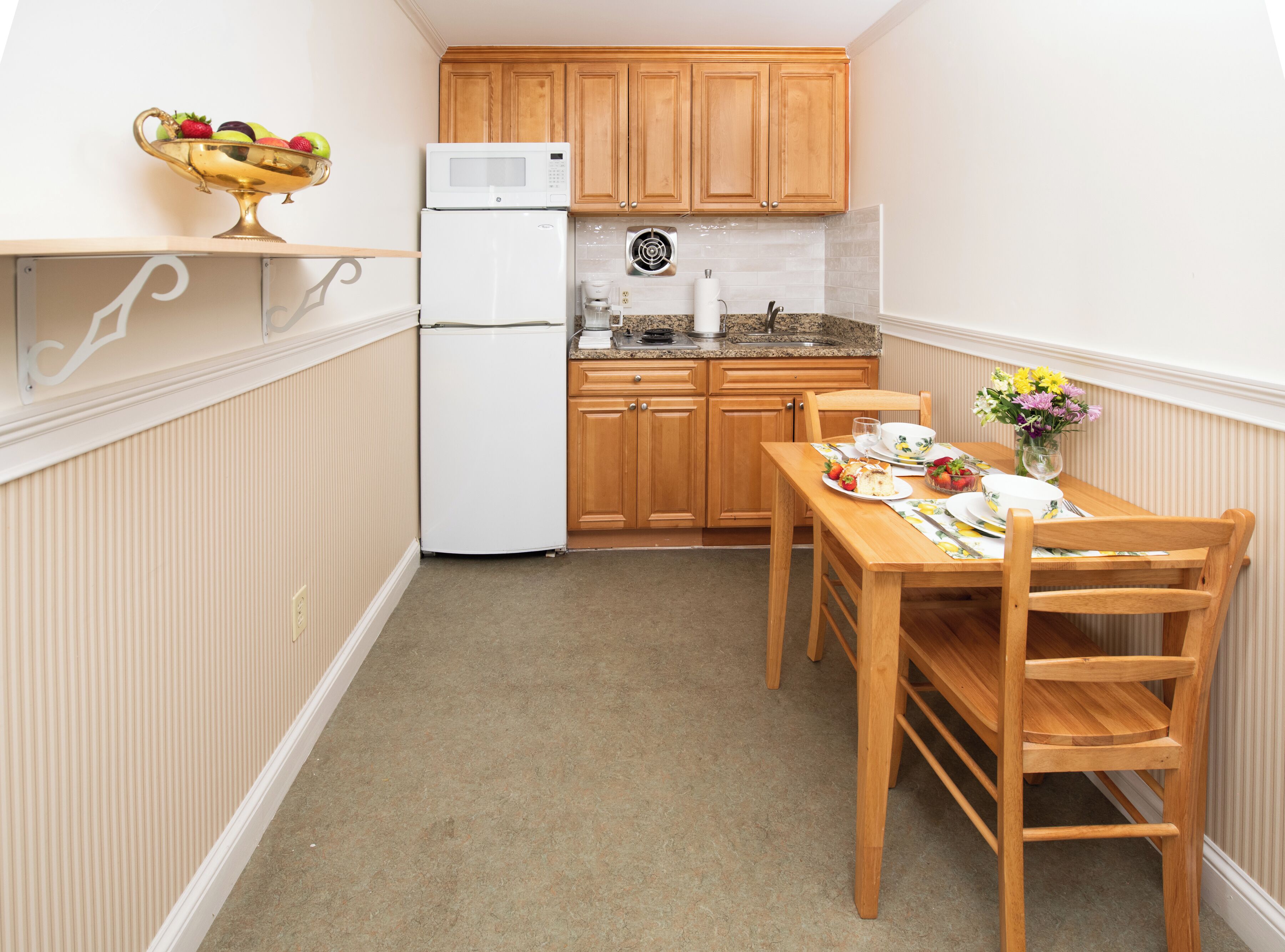 A compact kitchen with wooden cabinets, a white refrigerator, a microwave, and a dining table set for two.