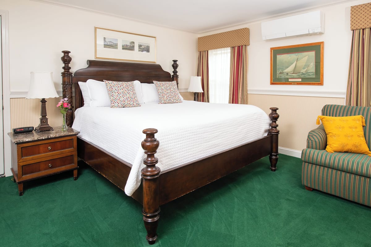 A neatly arranged bedroom with a large bed, a nightstand, a chair, and two framed pictures on the wall.