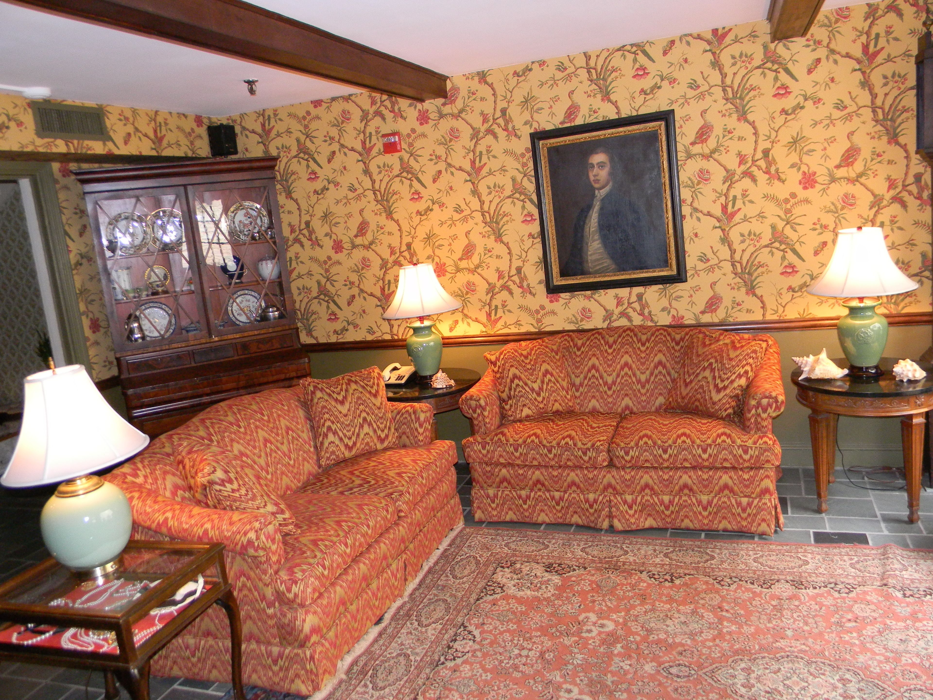 A traditional room with two sofas, a patterned rug, a wooden cabinet with glass doors, and a framed portrait on the wall.