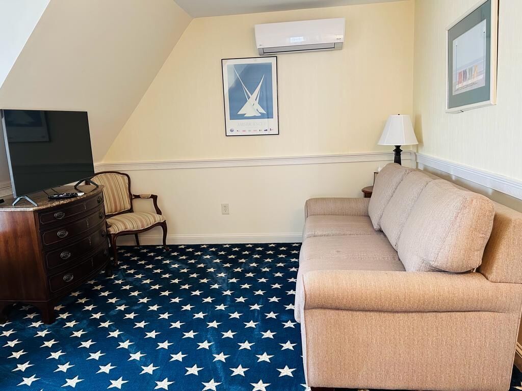 Una habitación con un sofá color beige, un aparador de madera, una silla y un televisor. El piso presenta un diseño con motivos de estrellas.