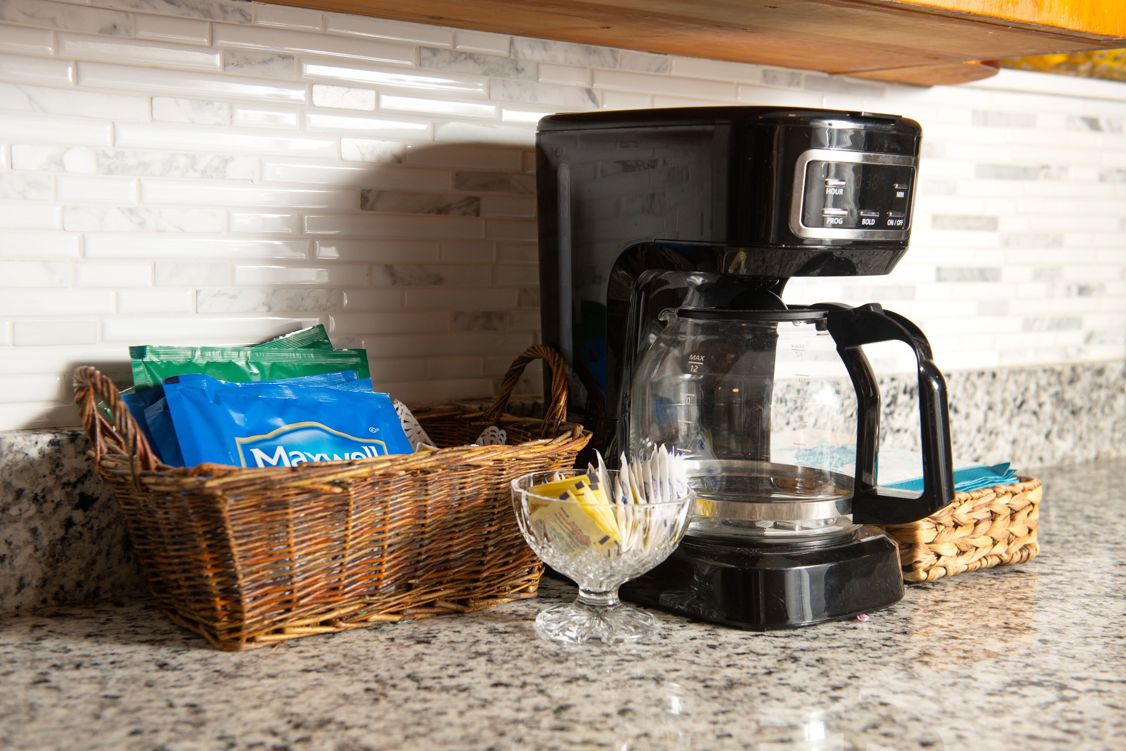 A kitchen counter with a coffee maker, wicker baskets, and a glass bowl.