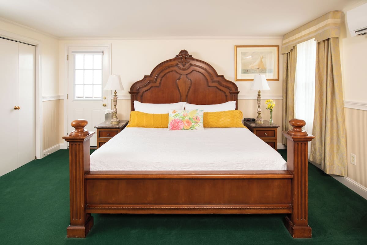 A neatly made bed with a wooden headboard, two bedside tables with lamps, and a green carpeted floor.