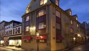A multi-story building with a prominent clock on the facade, a red awning, and a sign for a restaurant or cafe. - Americas Cup Inn (Newport)