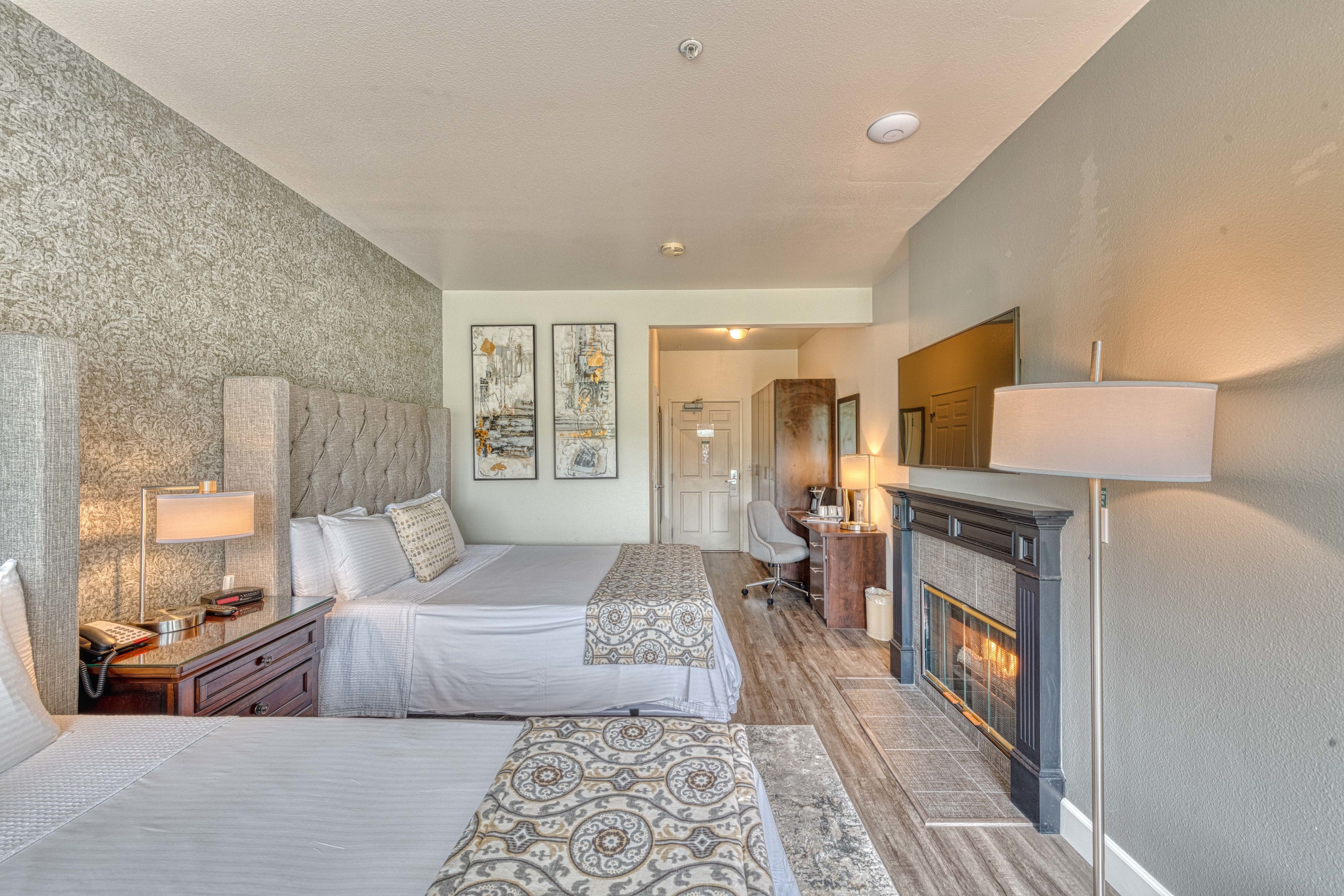 A hotel room with two beds, a fireplace, a desk, and a chair.