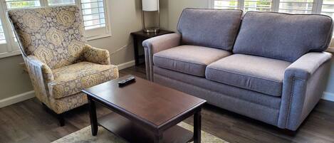 Una sala de estar con un sillón estampado, un sofá gris, una mesa de centro de madera y una lámpara de pie.