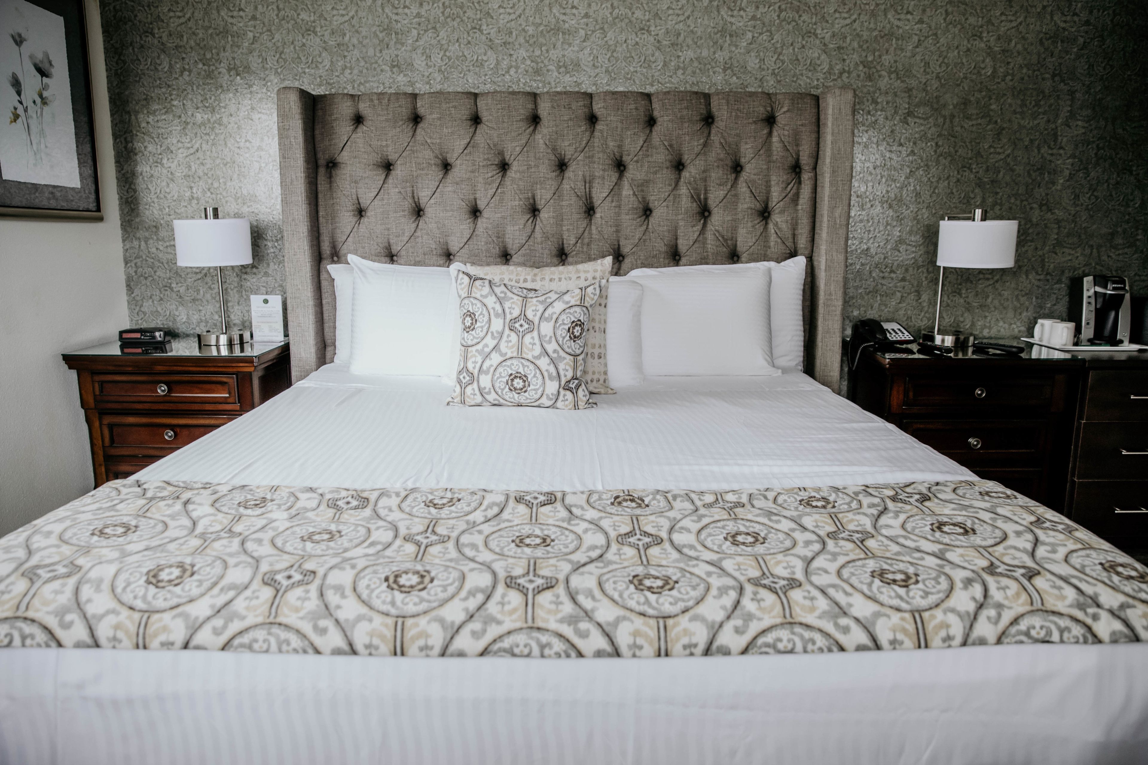 A neatly made bed with a patterned bedspread, a tufted headboard, and two bedside tables with lamps and a phone.