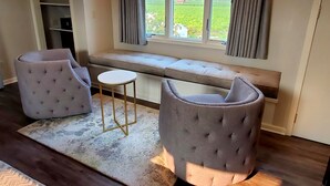 Quarto estilo loft com uma janela grande, um banco, duas poltronas e uma mesa pequena.