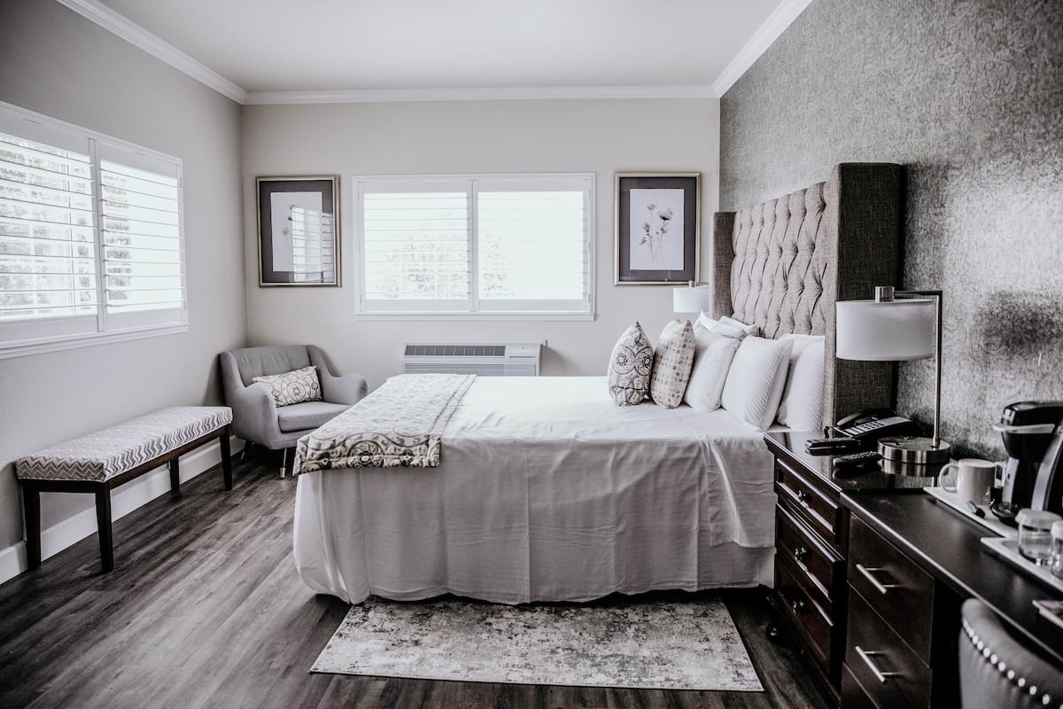 A modern bedroom with a large bed, a bench, a desk, and a dresser.