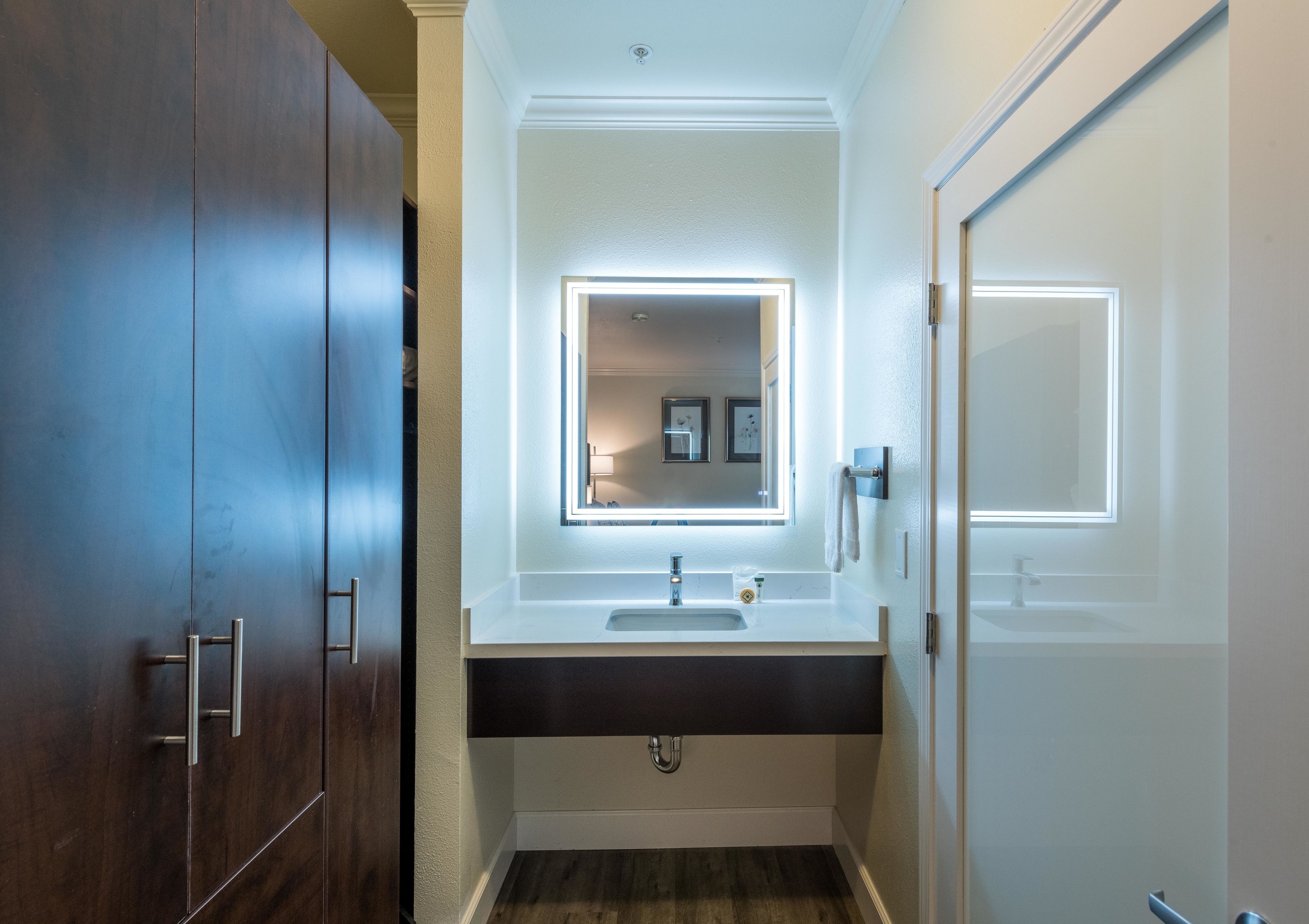 A bathroom with a dark wood vanity, a white sink, and a mirror with built-in lighting.