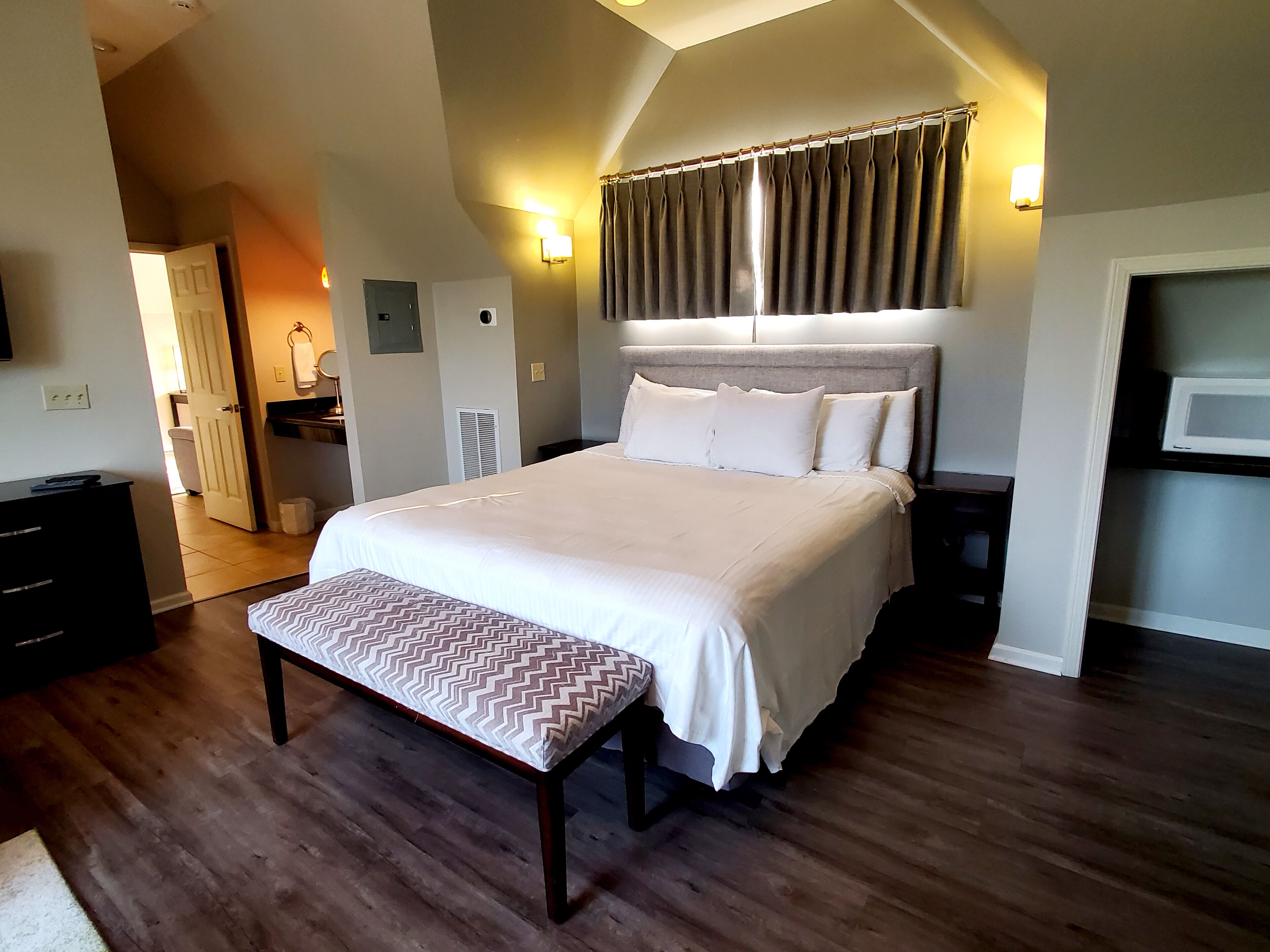 A bedroom with a large bed, a bench, a dresser, and a TV.