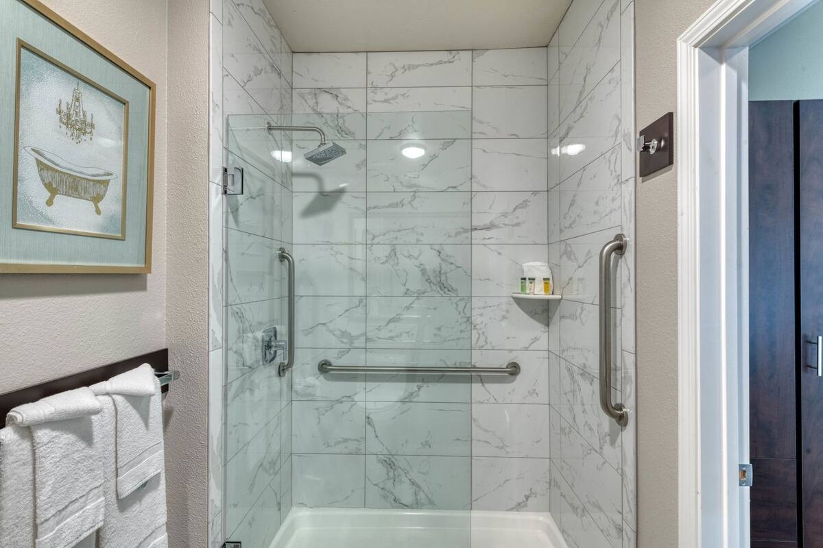 A bathroom with a glass-enclosed shower, marble tiles, a towel rack, and a framed picture on the wall.