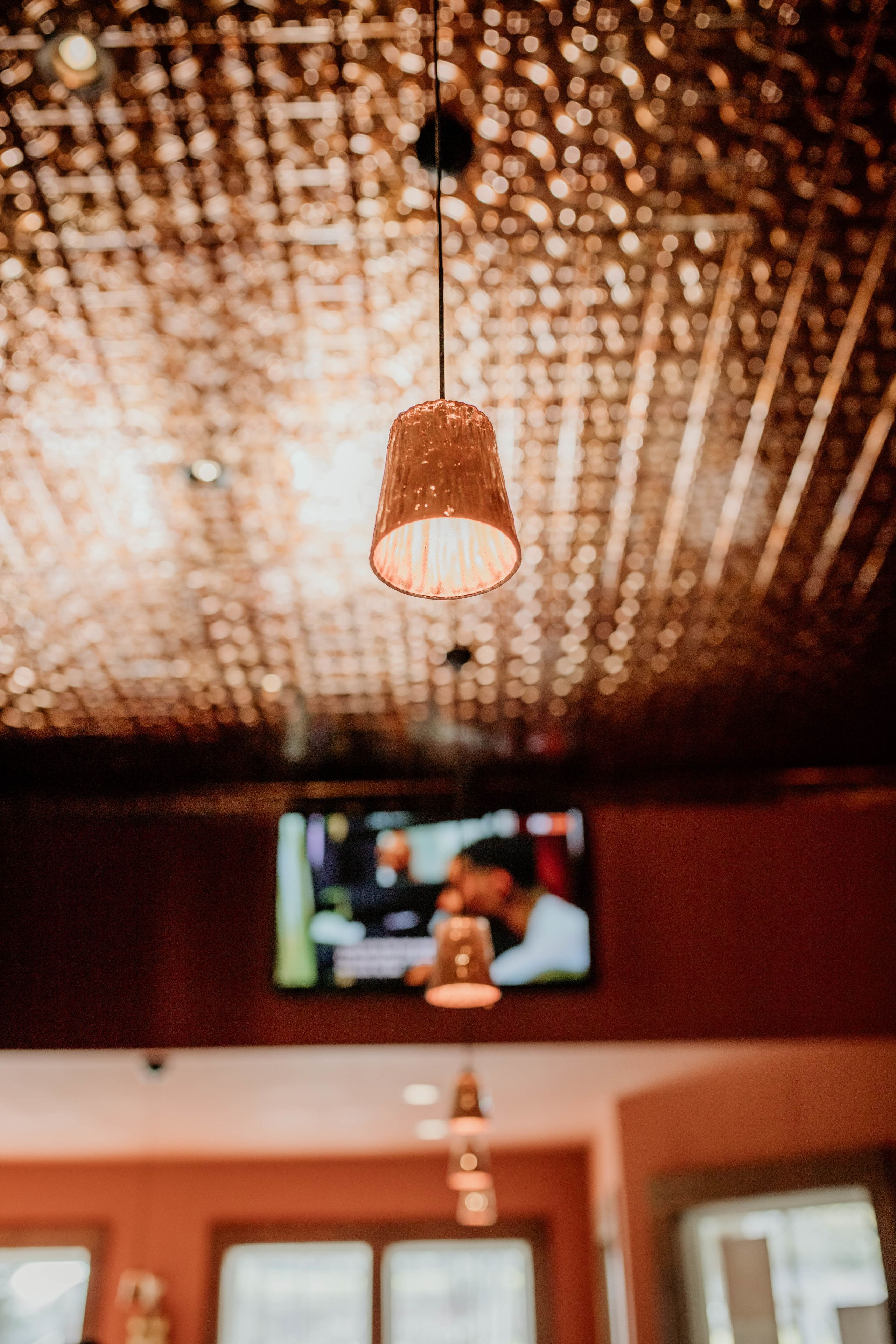 A ceiling with a decorative pattern of lights, a hanging pendant light, and a television screen in the background.