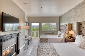 A hotel room with a fireplace, two beds, a large TV, and a balcony with a view.