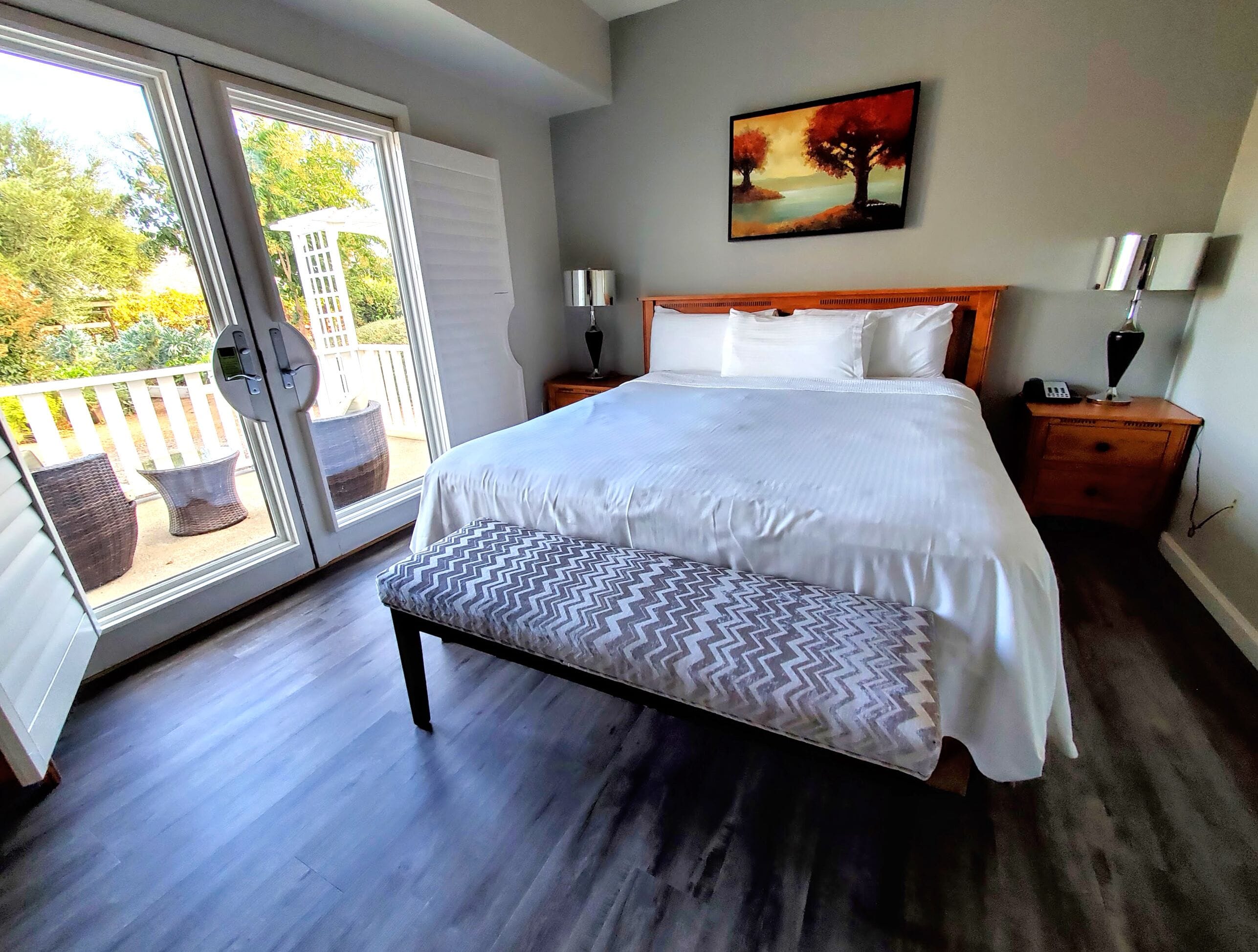 A bedroom with a large bed, a bench, a nightstand, a lamp, and a painting on the wall.