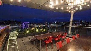 An outdoor seating area with a long wooden table and red chairs, surrounded by a railing and under a canopy of string lights. - Latroupe Jacobs Inn (Dublin)