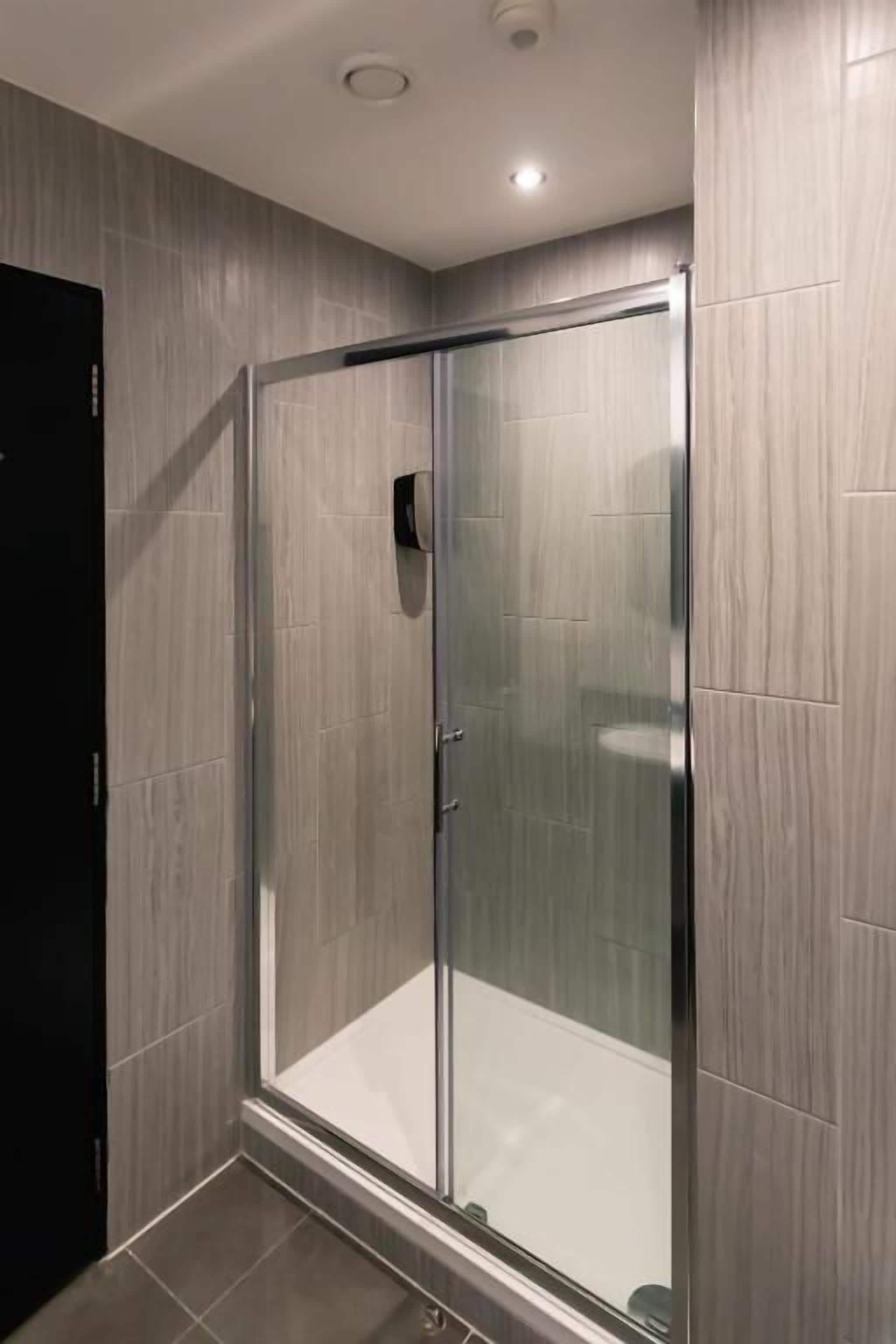 A modern bathroom with a glass-enclosed shower, tiled walls, and a dark door.