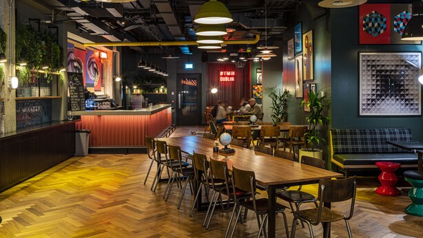 A modern restaurant with a wooden floor, multiple dining tables, and chairs. There are hanging lights and a bar area in the background. - Latroupe Jacobs Inn (Dublin)