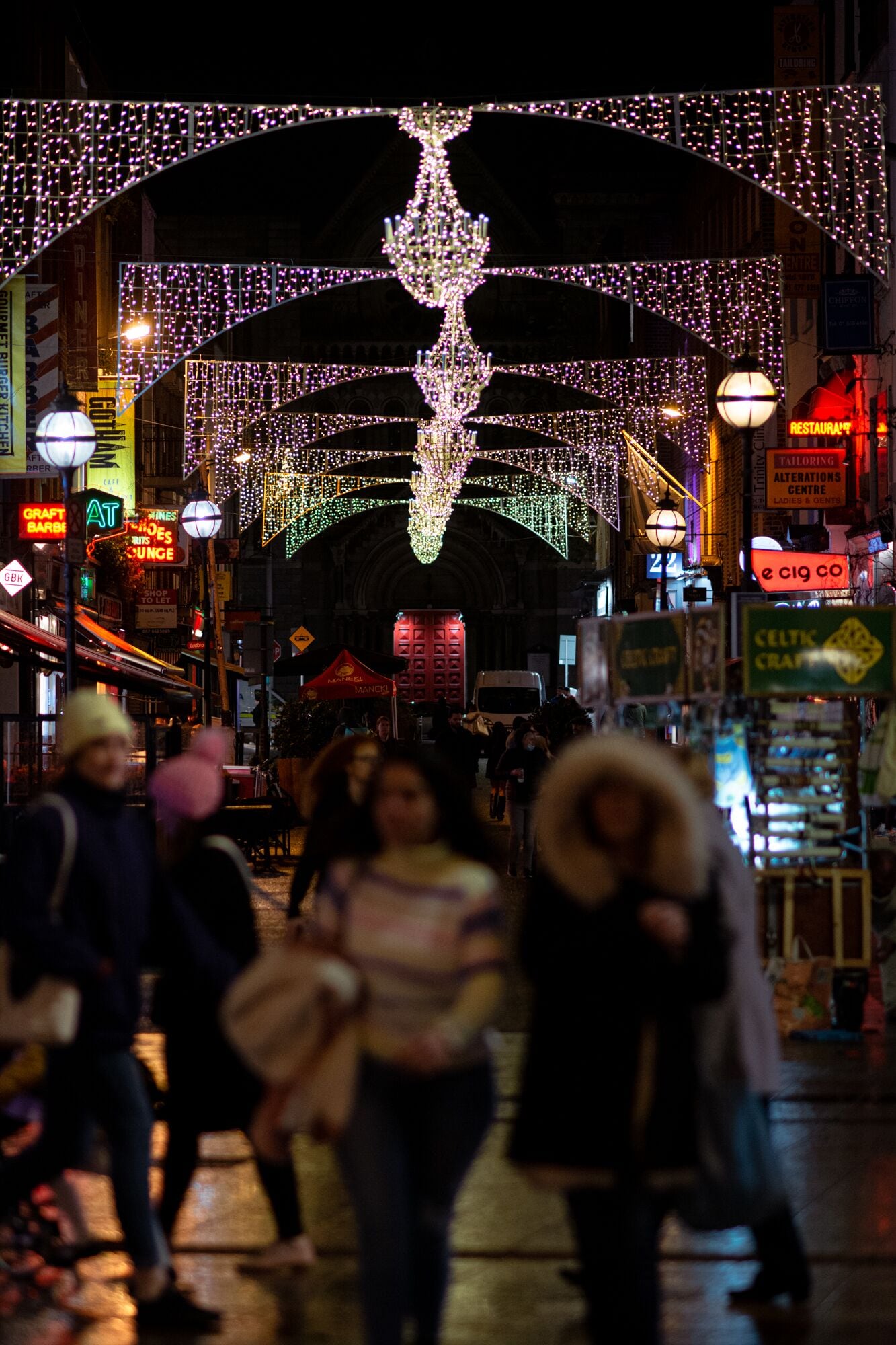 A busy street at night with illuminated arches and a large chandelier.