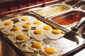A breakfast station with multiple fried eggs on a tray.