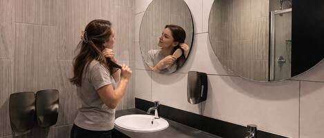 A modern bathroom with two sinks, a large mirror, and a towel dispenser.