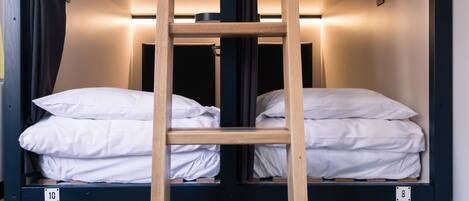 A bunk bed with a wooden ladder, white bedding, and a black metal frame.