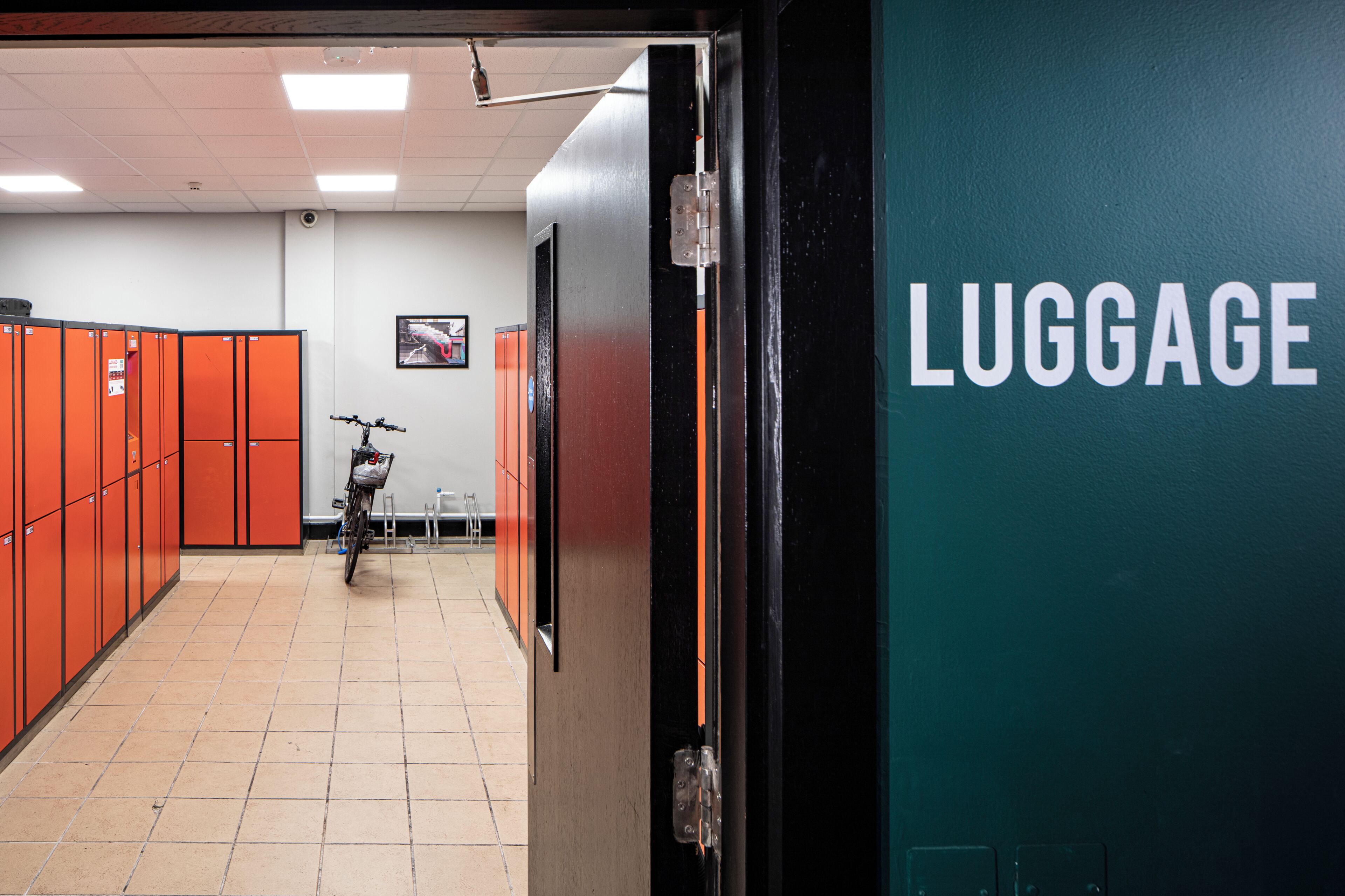 A hallway with orange lockers, a bicycle, and a wall labeled 'LUGGAGE'.