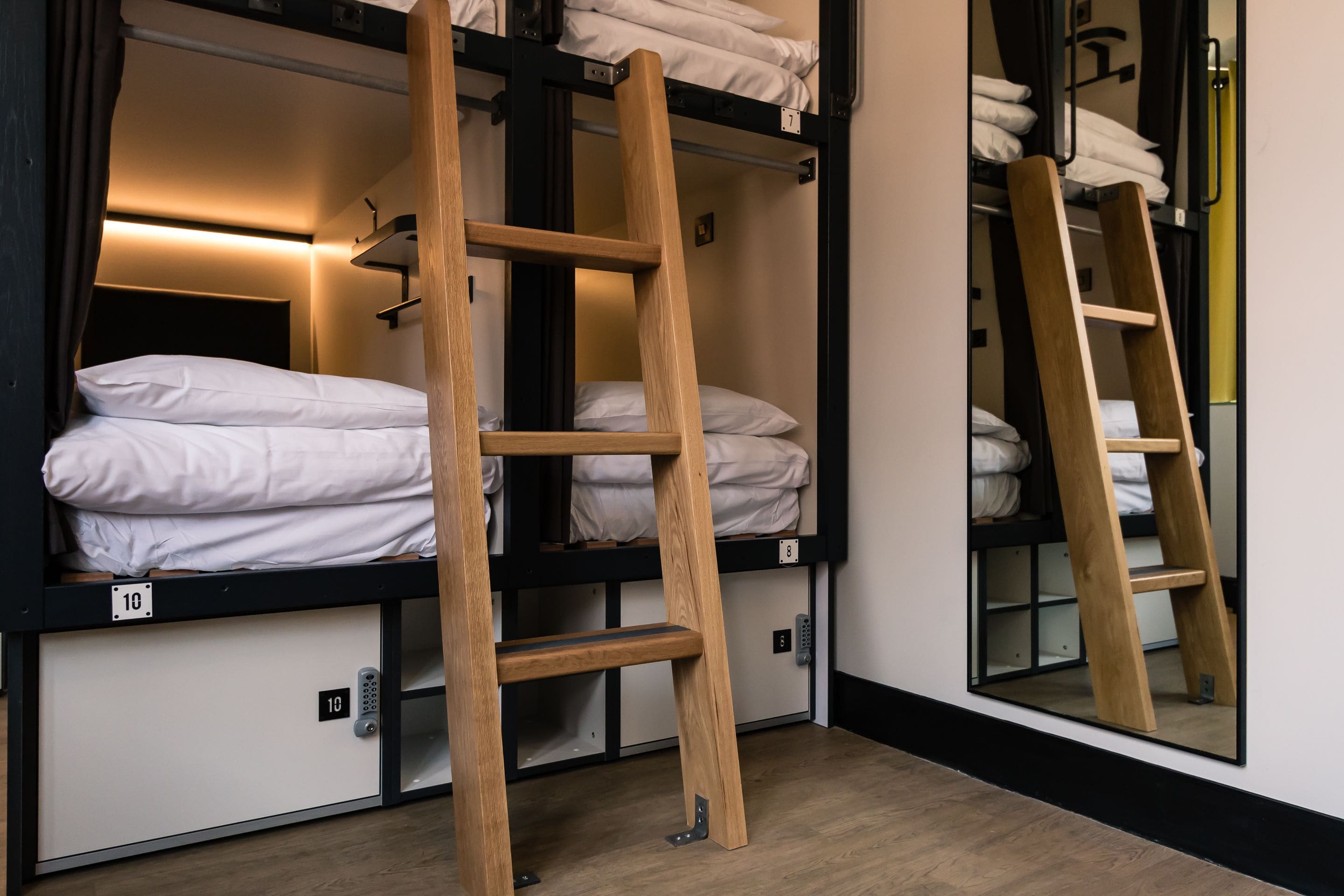 Bunk beds with wooden ladders, white bedding, and a mirror reflecting the room.