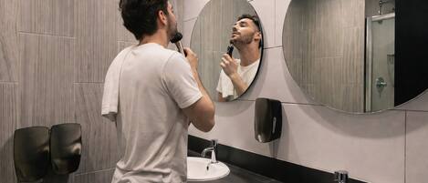 A modern bathroom with a large mirror, two sinks, and a towel dispenser.