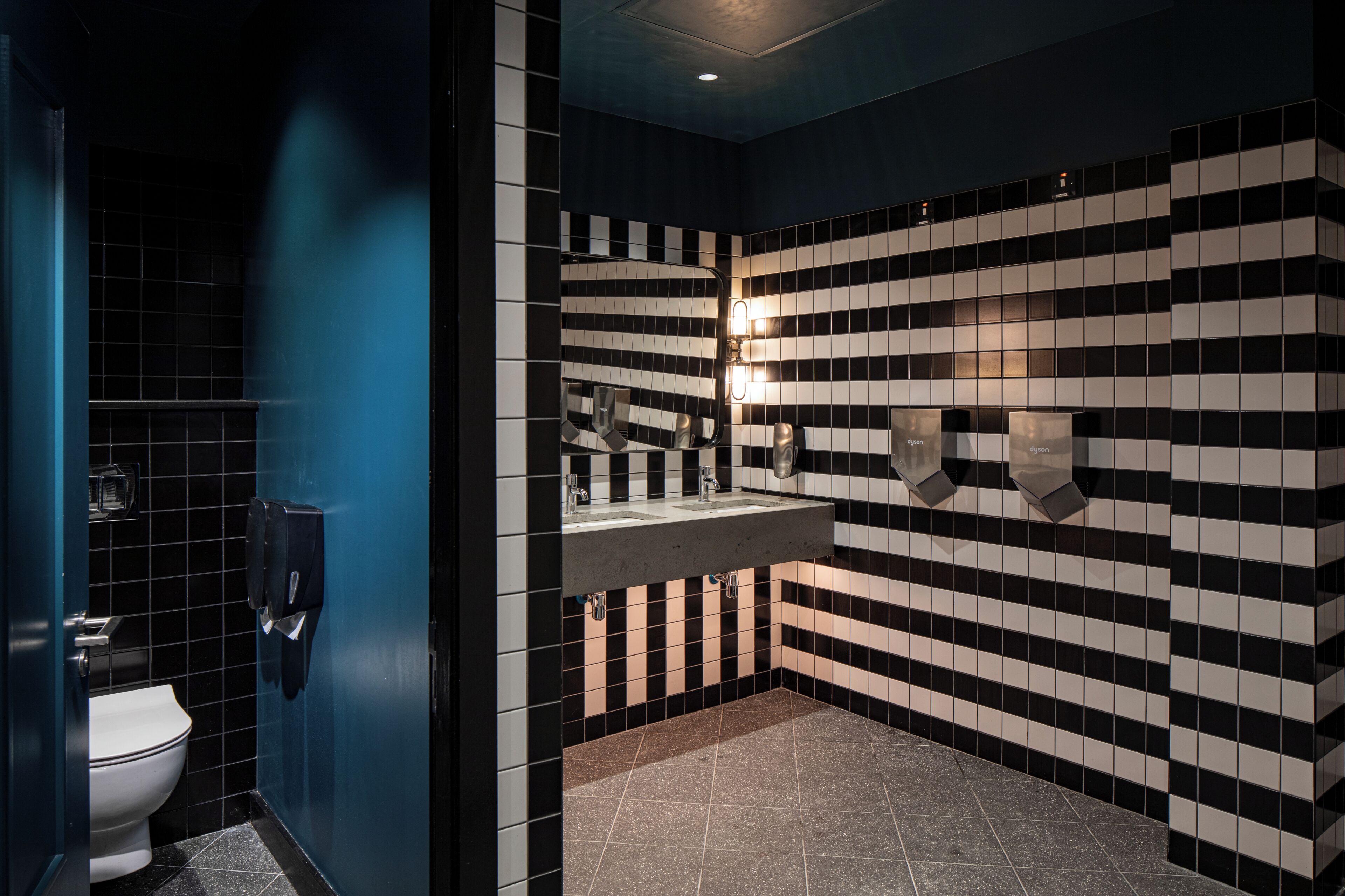 A bathroom with a black and white checkered wall pattern, a white toilet, and a sink with a mirror.