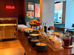 Buffet de café da manhã com diversos alimentos e acompanhamentos, uma placa indicando 'Dublin' e vista da rua.