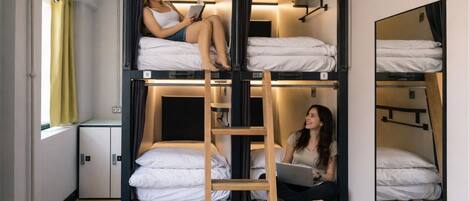 A bunk bed room with a ladder, a window with curtains, and a desk with a chair.