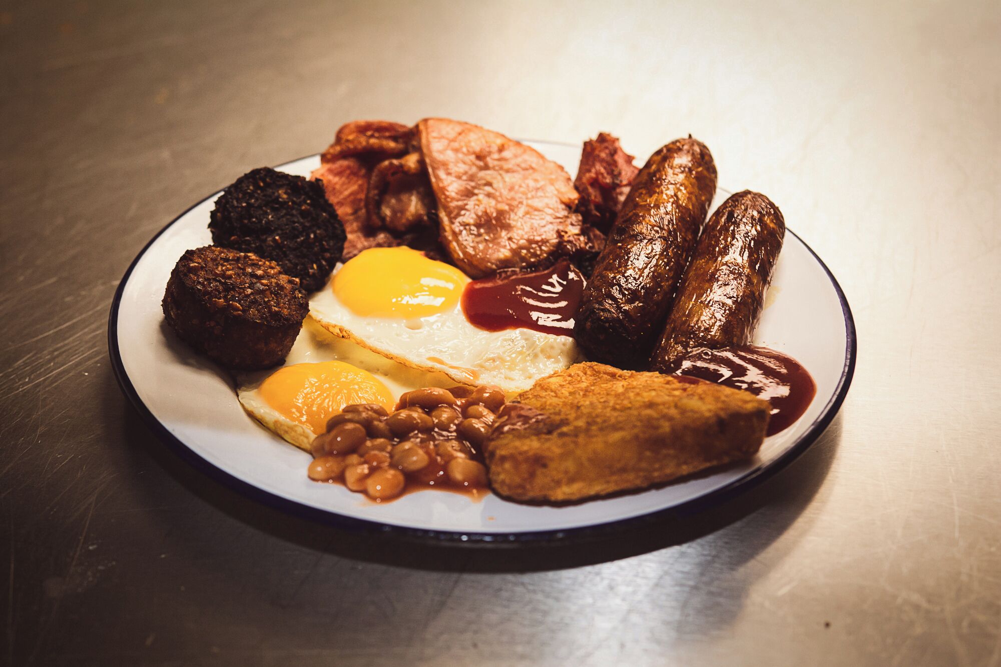 Une assiette de nourriture pour le petit-déjeuner comprenant des œufs, des saucisses, des haricots et des toasts.