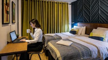 Habitación de hotel con escritorio, computadora portátil, dos camas y una cortina verde.
