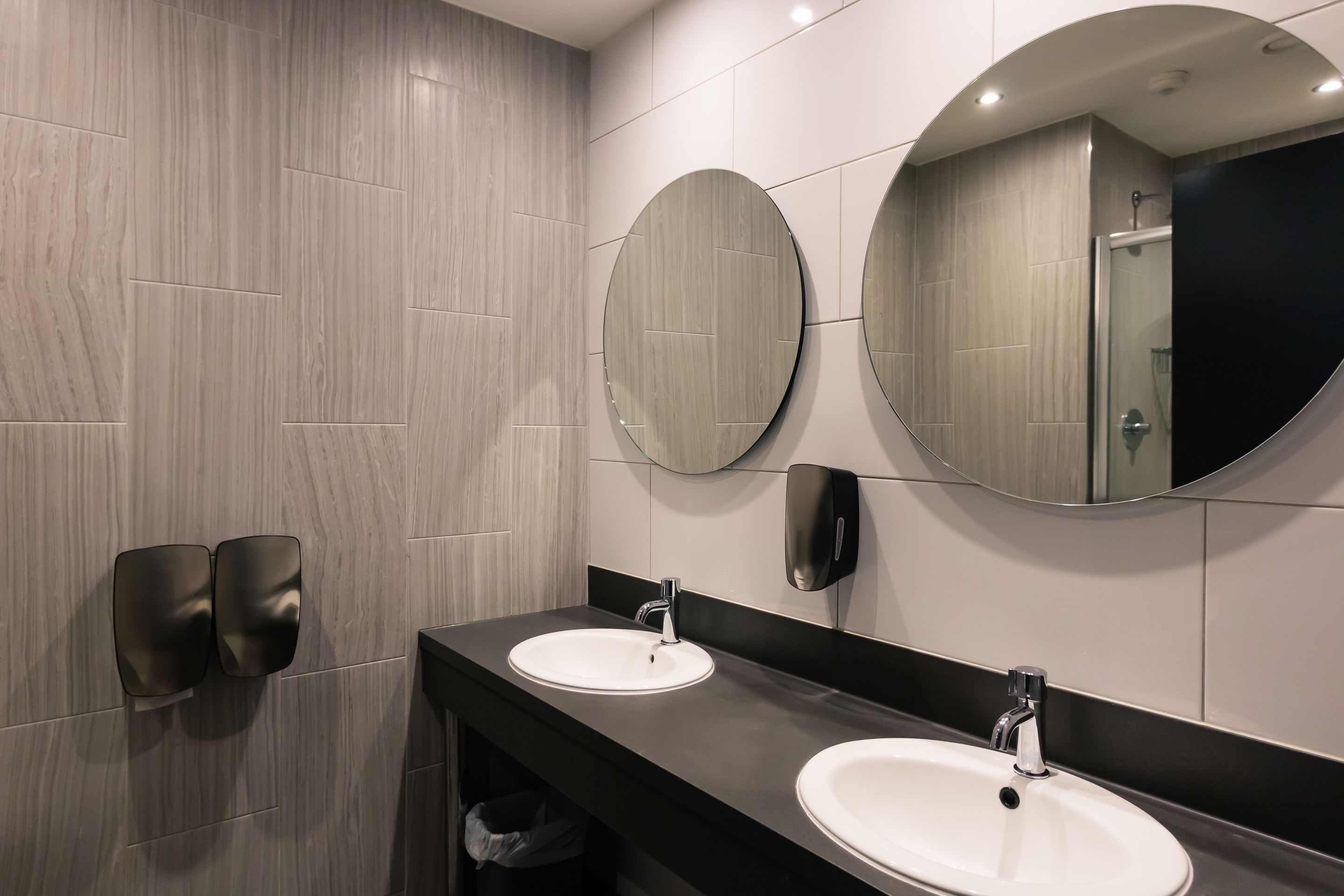 A modern bathroom with two sinks, a large mirror, and a hand dryer.