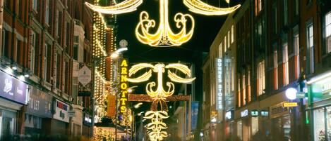 Una calle bordeada de edificios, decorada con letreros y luces iluminadas, y algunas personas caminando.