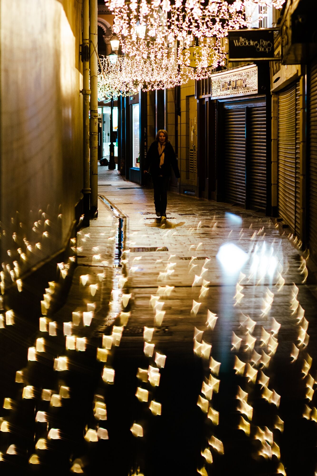 A corridor with a person walking, decorated with hanging lights and reflective surfaces.