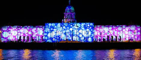 A building with a large dome and arched windows, illuminated with colorful lights reflecting on the water.