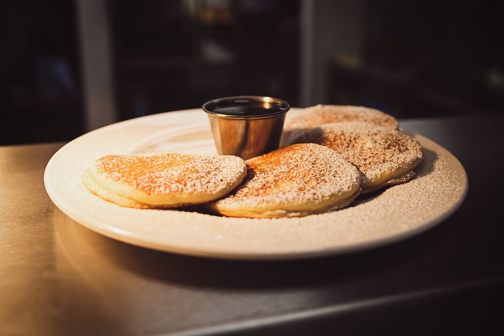 Una pila de tortitas con una taza pequeña de almíbar.